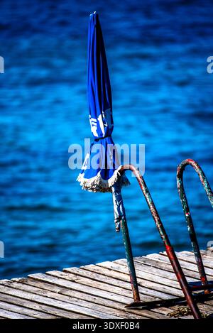 Ombrello blu bianco abbandonato sul molo di Torri del Benaco vicino al Lago di Garda Verona Veneto Italia Foto Stock
