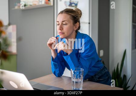 Concentrata sulla donna freelance che lavora su un laptop con schermo che riflette l'idea di un progetto che tiene la penna al lavoro da casa Foto Stock