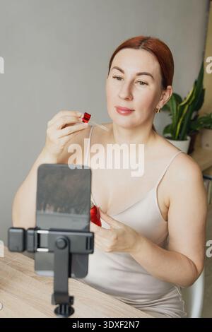 Donna che crea un vlog di bellezza che applica siero per la cura della pelle a casa Foto Stock