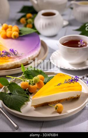 Cremosa fetta di cheesecake a strati condita con vivace gelatina di mango e lamponi gialli, che serve una deliziosa esperienza di dessert con un intero abbinamento Foto Stock