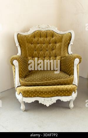Un'elegante poltrona in stile vintage in un angolo. Tappezzeria in velluto tufted verde Chartreuse e una cornice bianca decorata e intagliata. Luce soffusa in un design minimalista Foto Stock