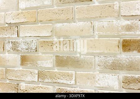Vista ravvicinata e angolata di una parete in mattoni con profondità di campo ridotta. La luce soffusa e luminosa evidenzia tonalità calde e neutre di beige, crema e ta Foto Stock