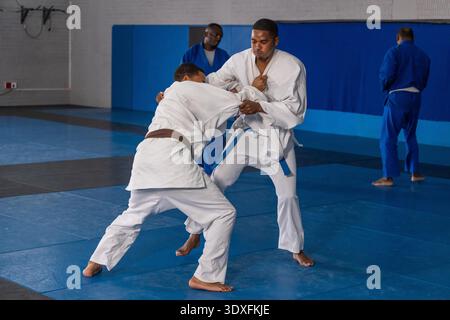 Diversi partner maschili con giacche di presa gis bianche e pratica nel dojo su tappetini blu. Martialarts, fitness, tradizionale, allenamento, atletica, disciplina, sport || modello rilasciato Foto Stock
