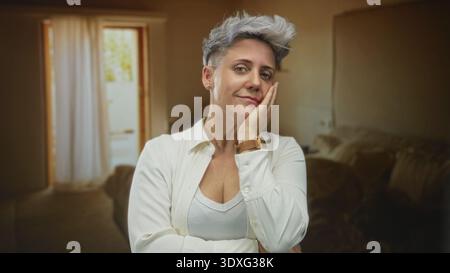 Donna con capelli corti che indossa una camicia bianca tiene mano alla fronte nell'edificio, in piedi davanti alla porta e alla tenda; imbarazzo. Foto Stock