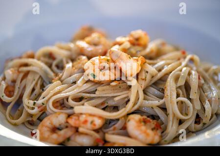 Linguine aglio e olio con gamberi cotti, aglio ed erbe aromatiche servite su un piatto bianco. La pasta è preparata con olio d'oliva e condimento. Foto Stock