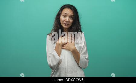 Donna che preme le mani sul petto con gli occhi chiusi in uno sfondo di studio color verde acqua, mostrando un gesto espressivo e sincero di sincerità e sollievo; premuroso Foto Stock