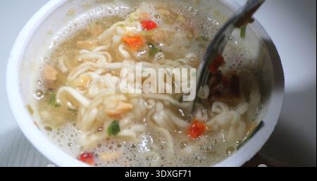 Ciotola calda di spaghetti istantanei con verdure e brodo in una tazza bianca durante lo spuntino serale Foto Stock