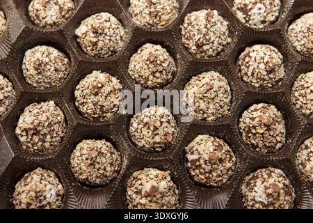 Vista dall'alto verso il basso delle caramelle al cioccolato con noci tritate in una scatola marrone. I tartufi rotondi creano uno schema ricorrente. Concetto di dessert gourmet per le vacanze, Foto Stock