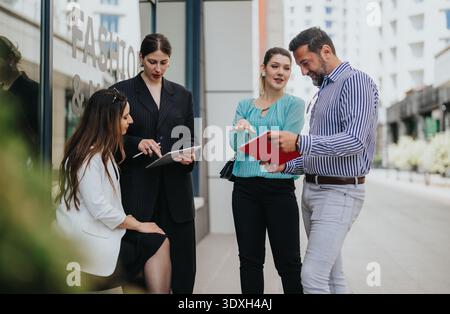 I colleghi aziendali si incontrano all'aperto, esaminano documenti e discutono insieme i piani di progetto Foto Stock