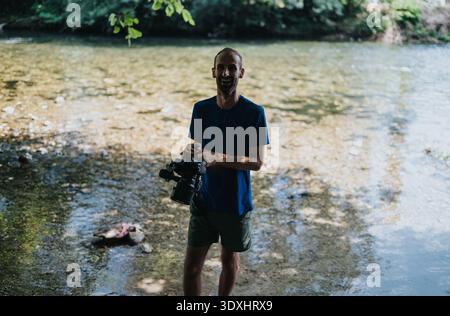 Uomo con macchina fotografica sul lungofiume che indossa una camicia della NASA, sessione fotografica all'aperto Foto Stock