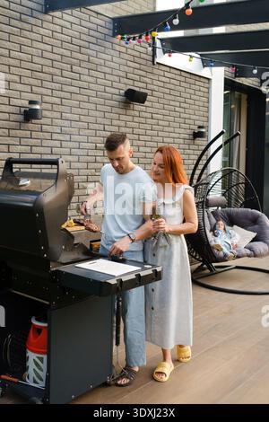 Due amici stanno cucinando al barbecue in un cortile in una giornata di sole. Condividono le risate e preparano il cibo per una piccola riunione mentre si godono Foto Stock