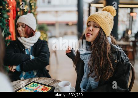 Due ragazze con abiti invernali si godono un momento di caffe' con un gioco da tavolo e un caffe' Foto Stock