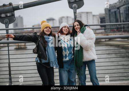 Tre ragazze posano su un ponte cittadino in inverno, sorridendo con sciarpe e cappotti Foto Stock