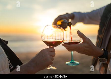 Versare vino rosso nei bicchieri durante il tramonto sulla spiaggia Foto Stock