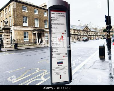 Londra, Regno Unito - 1 febbraio 2026: Londra, Regno Unito - 1 febbraio 2026: Un pannello informativo sulla fermata dell'autobus in una strada umida della città di Londra con edifici in mattoni Foto Stock