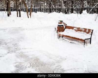panchina di legno nel giardino cittadino sgombra dopo le nevicate nella nuvolosa serata invernale Foto Stock