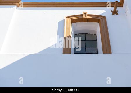 Un basso angolo e minimalista colpo esterno di un edificio in stucco bianco con una piccola finestra circondata da una cornice marrone Foto Stock