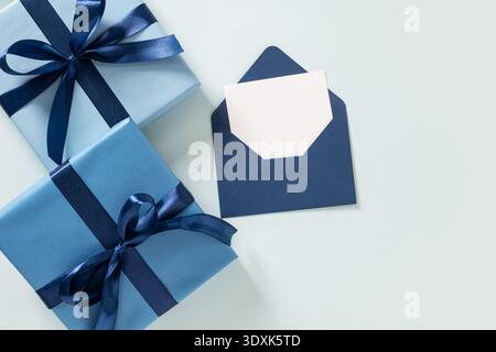 Confezione regalo blu con nastro e busta con carta bianca su sfondo pastello. Tema della Festa del papà. Composizione minima. Foto Stock