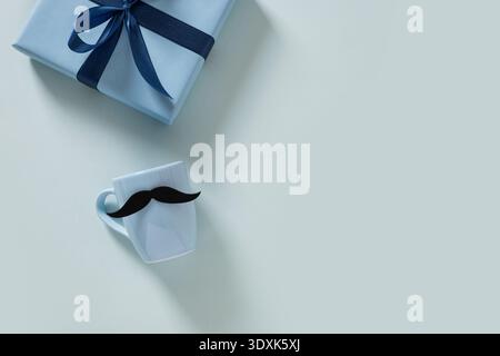 Tazza bianca con decorazioni di baffi e regali avvolti su sfondo pastello. Tema della Festa del papà. Stile minimalista. Foto Stock