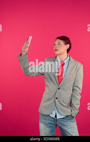 Persona che scatta selfie con lo smartphone su sfondo rosa Foto Stock