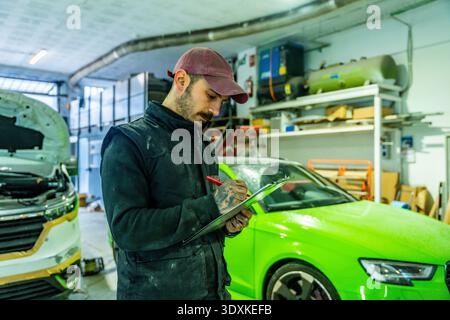 Meccanico che controlla i danni alla vettura nella carrozzeria Foto Stock