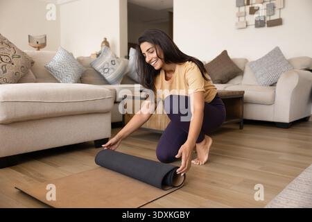 Donna che stende il tappetino per yoga, si prepara per l'allenamento a casa Foto Stock