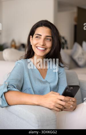 Donna seduta sul divano con un moderno smartphone Foto Stock