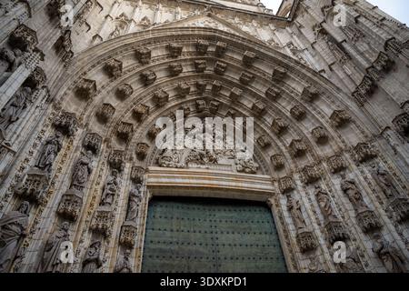 Vista ad angolo basso di una grande cattedrale gotica con arco in pietra scolpita e grande porta a Siviglia, Andalusia, Spagna. Dettagli architettonici spettacolari Foto Stock