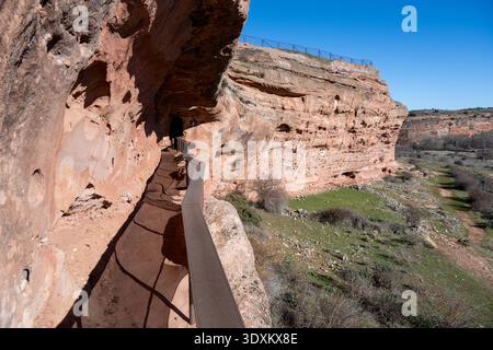 Passerella stretta con ringhiera lungo una scogliera di arenaria che conduce a un tunnel scavato nella roccia presso il sito archeologico di Tiermes a Soria, in Spagna. Foto Stock