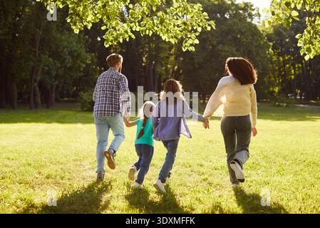Famiglia felice che si tiene per mano, corre sul green Field e si diverte a trascorrere il weekend insieme. Foto Stock