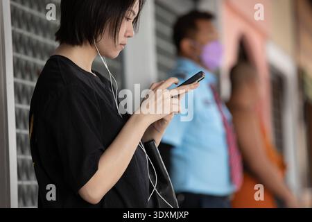 BANGKOK, THAILANDIA-FEB 4, 2026: Giovane donna che usa lo smartphone, assorbita dallo schermo mobile, utente di smartphone concentrato, profilo laterale, Wang Lang Foto Stock