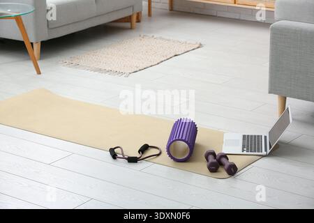 Rullo in gommapiuma con laptop, manubri e dilatatore per il fitness sul tappetino yoga nel soggiorno Foto Stock