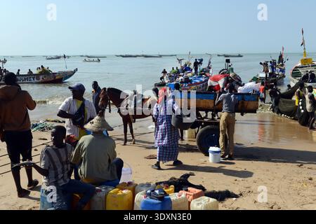 Un affollato mercato del pesce costiero con venditori ambulanti che vendono pesce fresco su una spiaggia di sabbia soleggiata a M'bour, Senegal. Foto Stock
