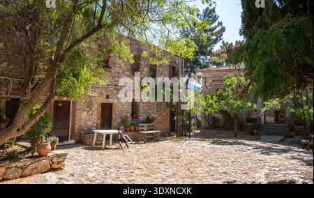 Edifici murali in pietra nel cortile del monastero di Nea Moni sull'isola di Chios, Grecia. Alberi e vasi di fiori in ceramica, cielo blu. Foto Stock
