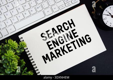 Testo di Search Engine Marketing scritto su blocco note con tastiera e sveglia su sfondo nero Foto Stock