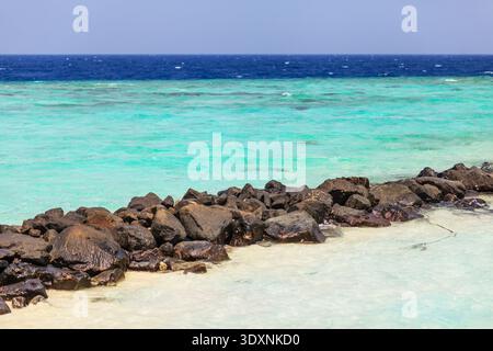 Le limpide acque turchesi incontrano rocce vulcaniche scure. Il mare poco profondo invita a un'esplorazione tranquilla vicino alla costa. Il sole luminoso si riflette su onde e sabbia dolci. Perfe Foto Stock