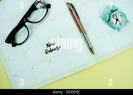 Nuovo messaggio di rilascio scritto sulla data del calendario con sveglia, lenti e lente d'ingrandimento su sfondo giallo Foto Stock