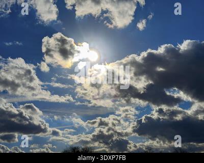 Guardando il sole dietro le nuvole, Cumulus si frattura contro un cielo blu, internazionale Foto Stock