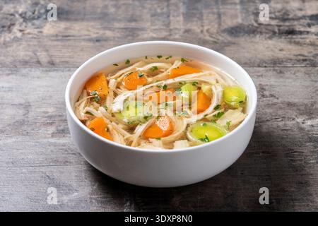 Zuppa di pollo fatta in casa in una ciotola bianca con carote e sedano su un tavolo di legno bianco Foto Stock