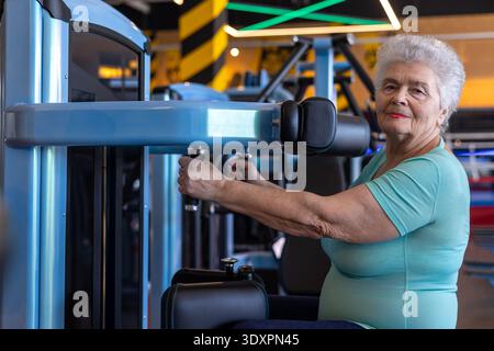Donna anziana sicura di sé oltre i 75 anni che pratica allenamento di forza in palestra, invecchiamento attivo e concetto di vita indipendente Foto Stock