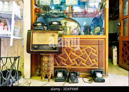 I visitatori esplorano un negozio di seconda mano a Damasco, in Siria, con vecchie radio e telefoni in esposizione. Il negozio propone vari articoli vintage. Foto Stock