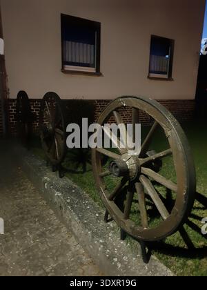 Le ruote di Ageold Wagon sono state appoggiate contro il muro in Moody Dusk Rural Environment with Moss and Shadows Foto Stock
