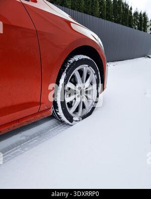 Ruota anteriore e parafango di un'auto rossa parcheggiata su un terreno innevato. Le tracce di usura degli pneumatici sono visibili nella polvere fresca dietro il veicolo. Foto Stock