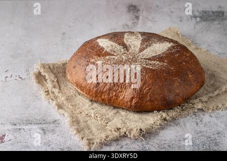 La pagnotta fresca di farro lievitata con semi di canapa tritati è decorata con foglie di cannabis fatte di farina su telo di lino su tavola di pietra grunge. Foto Stock