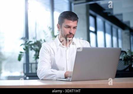 Un uomo è seduto a una scrivania con un portatile di fronte Foto Stock