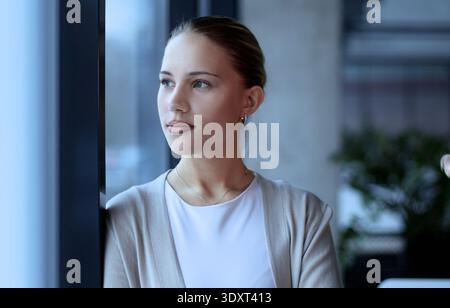 Una donna è in piedi davanti a una finestra con la mano sul mento Foto Stock