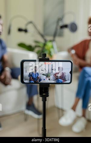 Gli ospiti africani registrano a casa con il telefono su treppiede, i microfoni con timer rosso, ospite medico Foto Stock