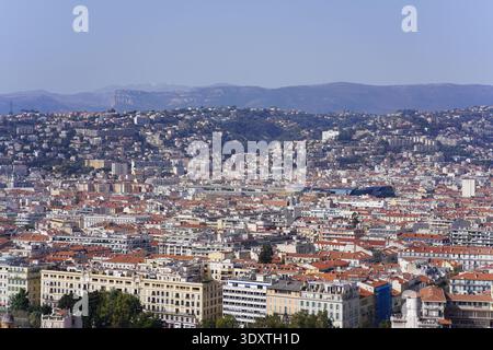 Didascalia: Ampia vista panoramica sul vibrante paesaggio urbano di Nizza con tetti in terracotta e fitti quartieri che si arrampicano sulle colline Foto Stock