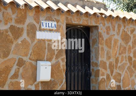 Una villa rustica in pietra a Torrevieja, Spagna, presenta un cancello nero in ferro battuto e una cassetta postale bianca, con la parola "VILLA" su un cartello sopra l'ingresso. Foto Stock