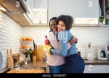 Giovani donne felici che abbracciano e ridono in cucina Foto Stock